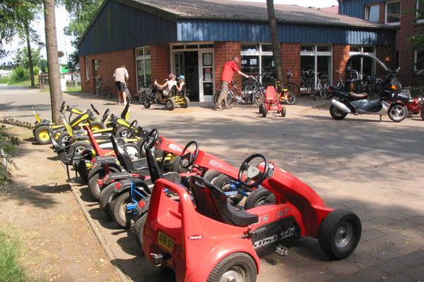 Røde go-karts foran Sudsee-Camp bygning med personer og cykler i baggrunden.