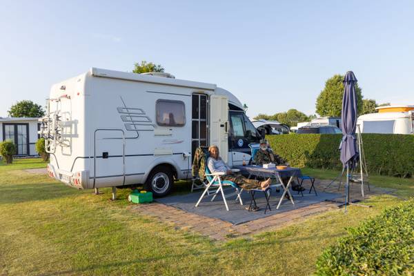 Dos personas descansando frente a una autocaravana blanca en Insel-Camp Fehmarn.