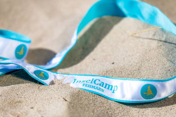 Primera plana de una pulsera blanca y azul del Insel-Camp Fehmarn sobre la arena.