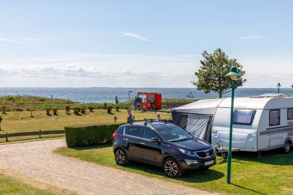 Un camping en Insel-Camp Fehmarn con un SUV negro y una caravana junto al océano.