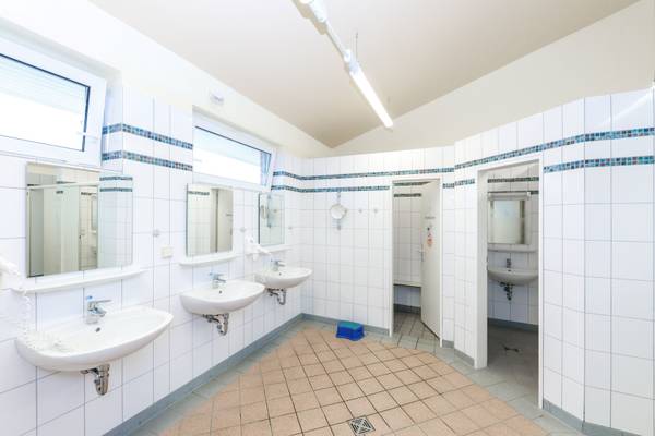 Baño en el Insel-Camp Fehmarn con azulejos blancos y tres lavabos.
