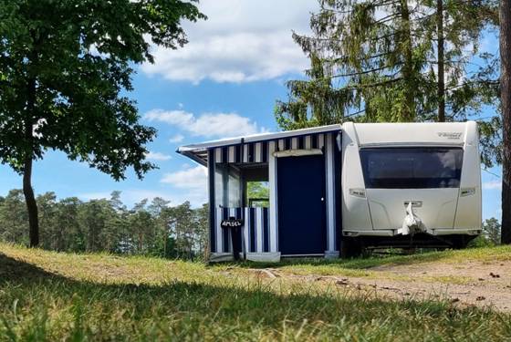 Hvid campingvogn med blå markise under træer på en skråning i Sydhavs-lejren