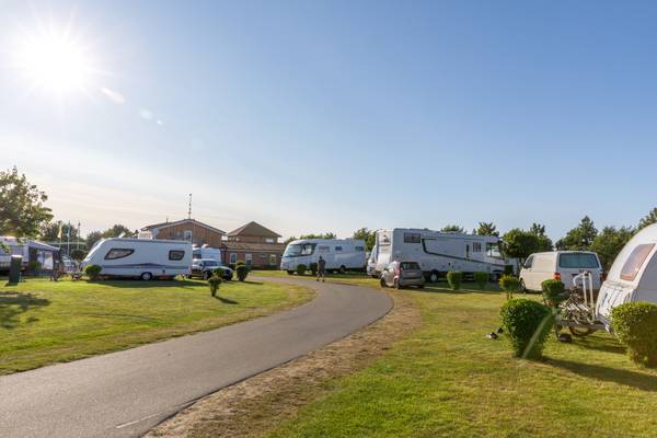 Camping Insel-Camp Fehmarn bajo el sol con varios autocaravanas estacionados en césped verde.