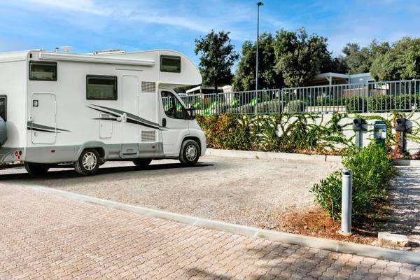 Un camping-car blanc garé au Camping Vestar, entouré de verdure et d'un chemin en brique.