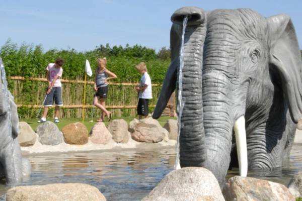 Campamento Jambo Feriepark con niños jugando cerca de una escultura de elefante y una fuente de agua.