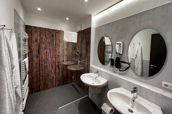 Baño con paredes de madera, dos lavabos y dos espejos, uno reflejando una toalla.