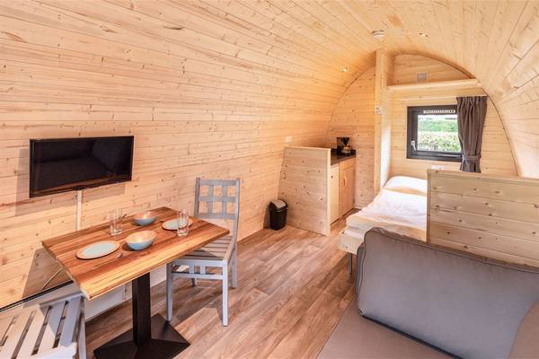 Interior de una casa de vacaciones con paredes de madera, un televisor de pantalla plana, una mesa con sillas y una cama.