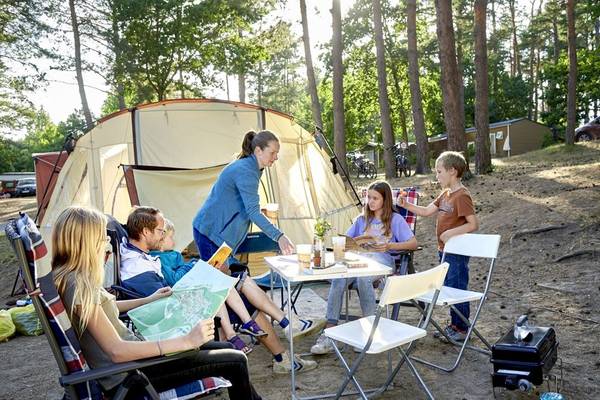 A family of five enjoys a picnic in front of a tent at the campsite.