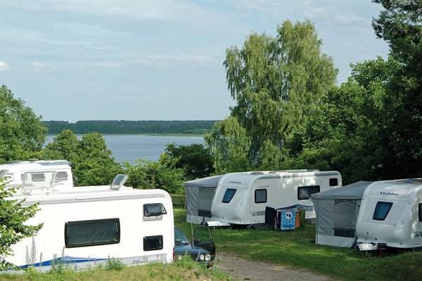Campsite with several white recreational vehicles parked by a lake under a blue sky.