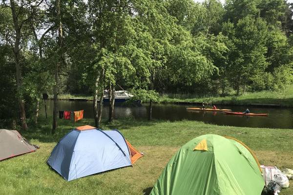 Three tents set up on grass near a river with trees and people kayaking