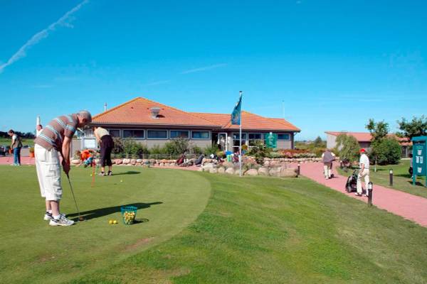 Golfer spielen auf dem Golfplatz Wulfener Hals mit dem Clubhaus im Hintergrund.