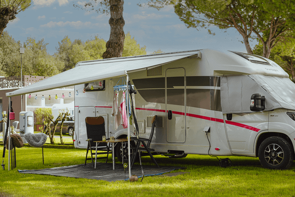 Een witte camper met luifel geparkeerd op een gazon bij bomen.