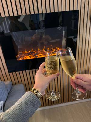 Dos personas sosteniendo copas de champán frente a una chimenea en el Feddet Strand Resort.