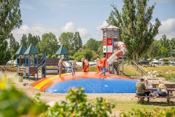Ein farbenfroher Spielplatz am Wulfener Hals Campingplatz mit spielenden Kindern und einer sitzenden Familie.