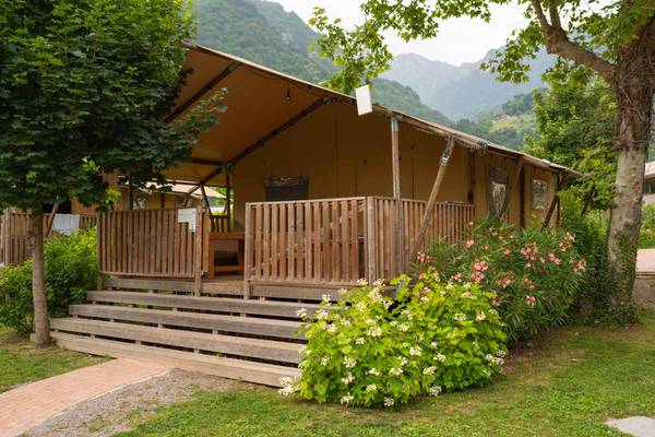 Tent de glamping avec terrasse en bois, entouré de fleurs et de montagnes.