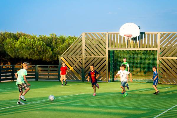 Enfants jouant au football sur un terrain vert au Camping Village Le Brasilia