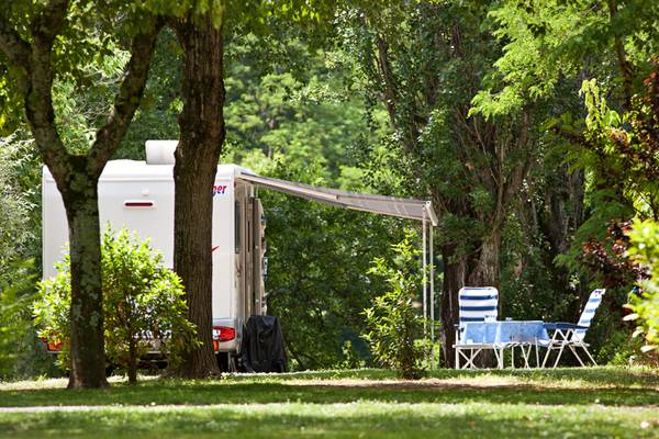 RV estacionado bajo los árboles con una toldo y sillas y mesa