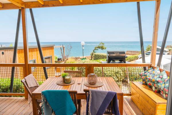 Terrasse mit Meerblick im Camping Les Criques de Porteils, mit Holztisch und Stühlen sowie einem Grill im Hintergrund.