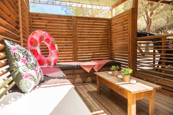Campingterrasse Sitzecke mit Dekoration, bestehend aus Holzwänden, einem Erdbeer-Schwimmring, Kissen und einem Tisch.