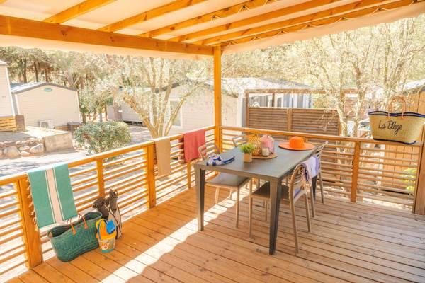 Camping-Terrasse mit Tisch und Stühlen, umgeben von Bäumen und Häusern.