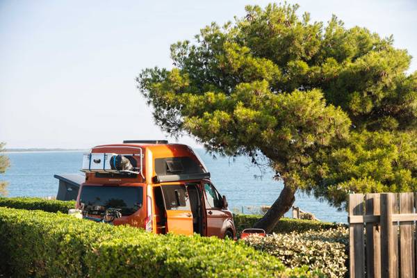 Oranger Camper unter einem Baum am Campingplatz Les Criques de Porteils am Meer.