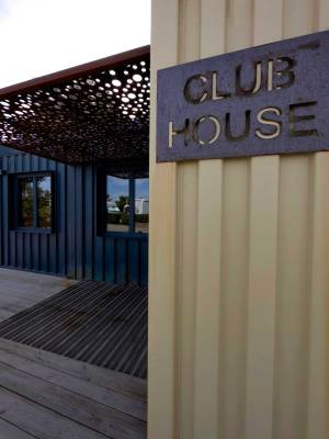 Eingang zum Club House im Camping Les Criques de Porteils mit einer Holzterrasse und einem Metallschild.