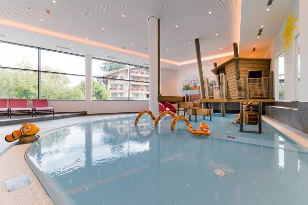 Piscina per bambini al Sportcamp Woferlgut con sedie rosse e casetta in legno.