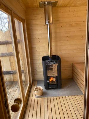 Holzsauna mit Ofen und Fenster, der Blick nach draußen ist sichtbar.