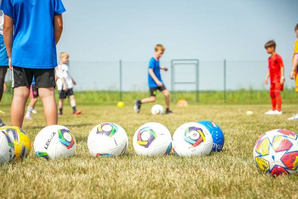 Entrenamiento de fútbol infantil en un campo de césped con varios balones de fútbol en primer plano.