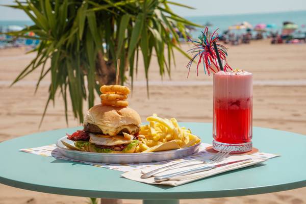 Comida rápida con hamburguesa, papas fritas y un cóctel en una mesa de playa.