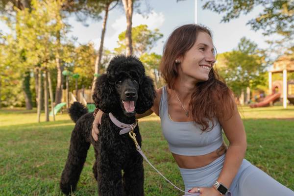 Mujer con un caniche negro sentado en el césped de un parque.
