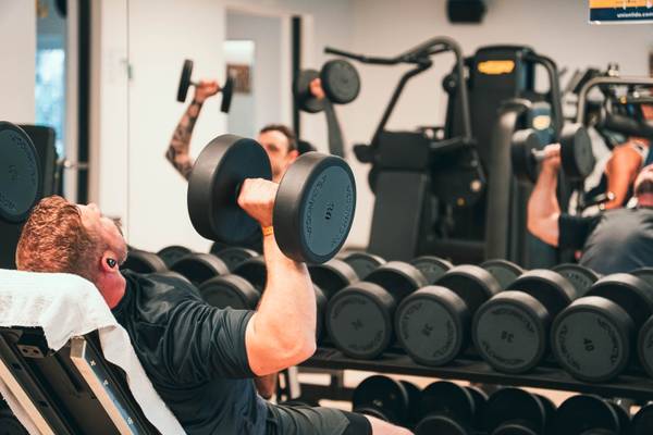 Hombre haciendo entrenamiento de fuerza en un gimnasio con mancuernas en primer plano.