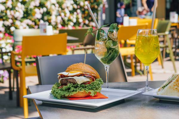 Hamburguesa, sándwich y bebidas en una mesa de un restaurante al aire libre.
