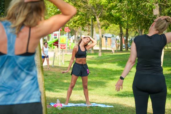 Mujeres haciendo yoga en el camping Union Lido Mare con árboles y parque infantil al fondo.