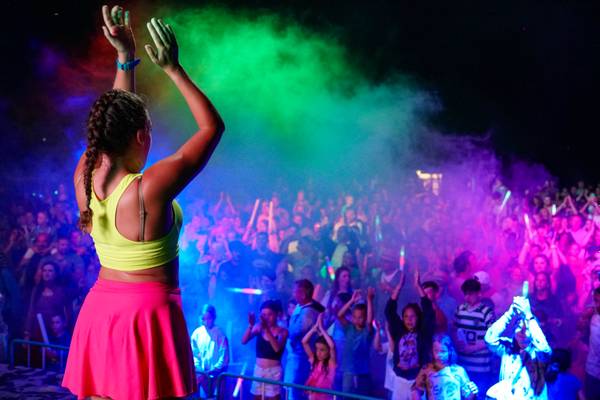 Mujer en un concierto con efectos de humo coloridos en el fondo.