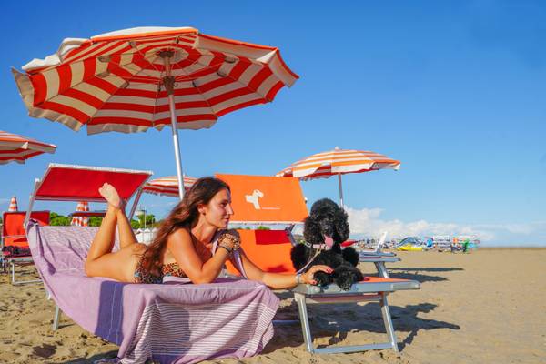 Mujer relajándose en una tumbona de playa con un poodle negro en un día soleado
