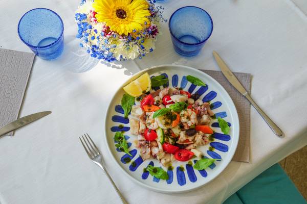 Un plato de ensalada de mariscos con tomates y albahaca sobre una mantelería blanca.