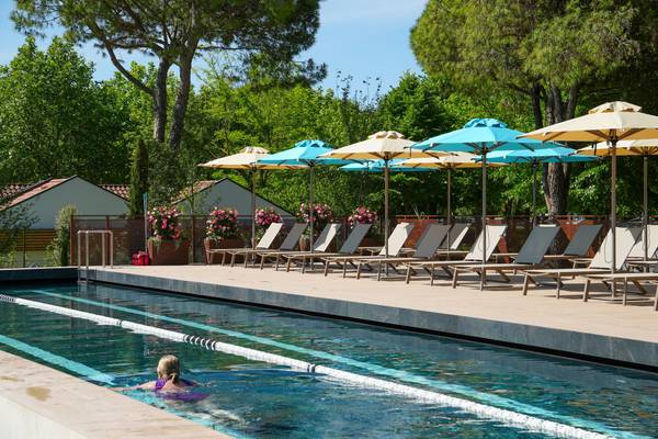 Mujer nadando en la piscina al aire libre del camping Union Lido Mare con tumbonas y sombrillas.