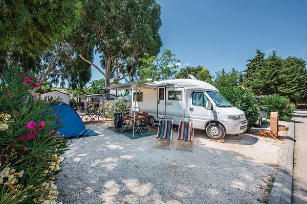 Campingplatz mit Wohnwagen und Zelt unter einem Vordach im Schatten von Bäumen.