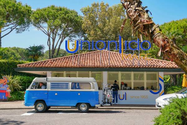 Una furgoneta VW azul y blanca estacionada frente al edificio del camping Union Lido Mare.
