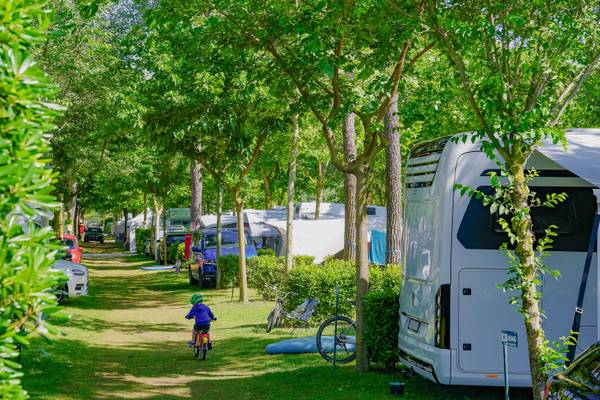 Niño en bicicleta frente al camping Union Lido Mare con árboles y vehículos estacionados.