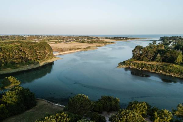 Vue aérienne du Camping Village L`Océan Breton, montrant une rivière, des arbres et la mer.
