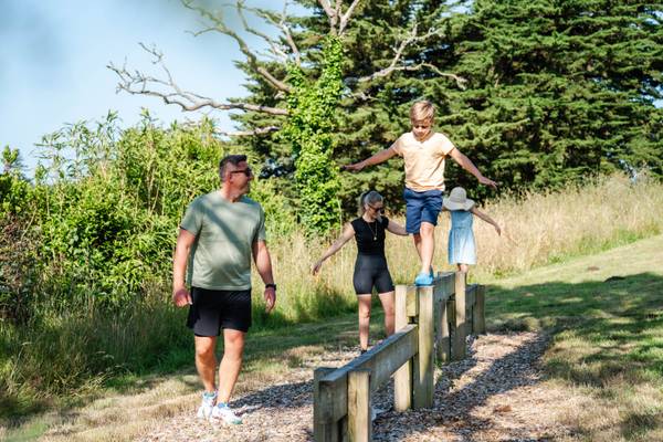 Famille marchant sur des bûches en bois au Camping Village L`Océan Breton avec des arbres hauts en arrière-plan