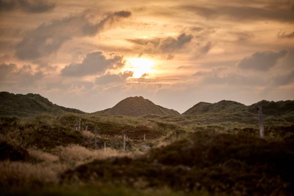 Sunset over dunes at Henne Strand Resort, a serene landscape with hills and clouds.