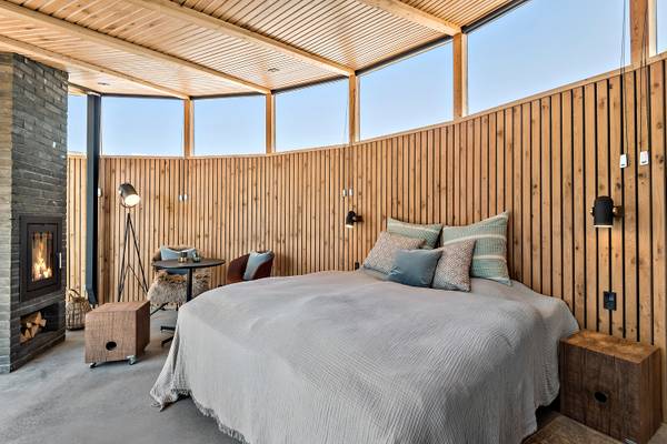Henne Strand Resort bedroom with wooden walls, bed, fireplace, and lamps.