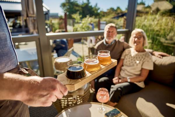 Waiter serving beers at Henne Strand Resort Campsite, with elderly couple in the background.