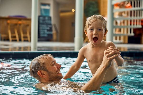 Man and boy swimming in pool with water splashing around