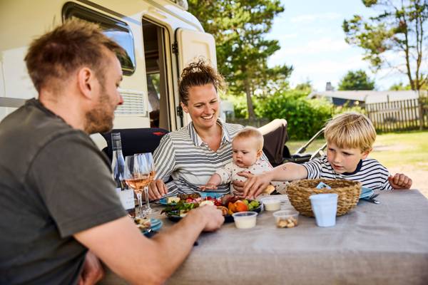 Family sitting at a table in front of their camper at Henne Strand Resort campsite.