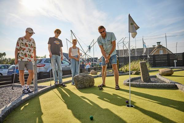 Four people play mini golf at Henne Strand Resort, with one man about to hit.