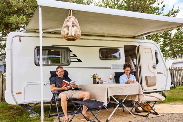 A couple sits in front of a white RV at Henne Strand Resort campsite.